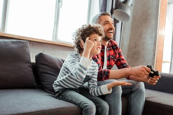 KYIV, UCRÂNIA - 14 de maio de 2020: pai feliz jogando videogame perto de filho descontente na sala de estar — Fotografia de Stock