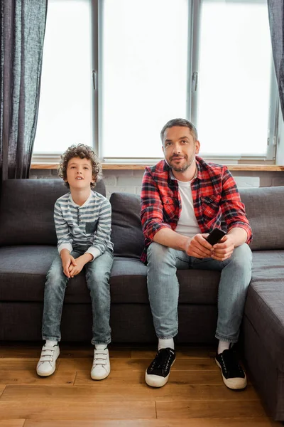 Schöner Vater und lockiger Sohn sehen Film im Wohnzimmer — Stockfoto