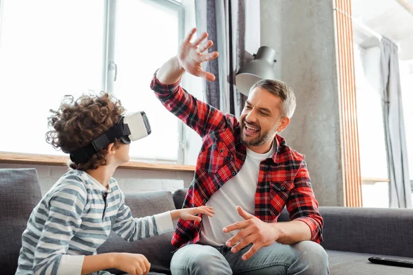 Feliz padre dando alta cinco a hijo rizado en auriculares de realidad virtual - foto de stock