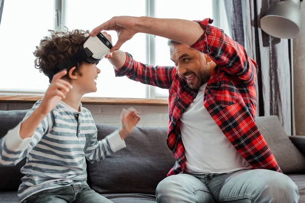 Felice padre toccando realtà virtuale auricolare sul figlio riccio — Foto stock