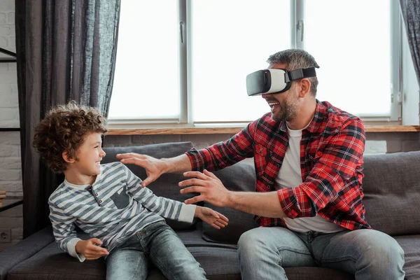 Веселий батько у гарнітурі віртуальної реальності жестикулює біля щасливого сина — стокове фото