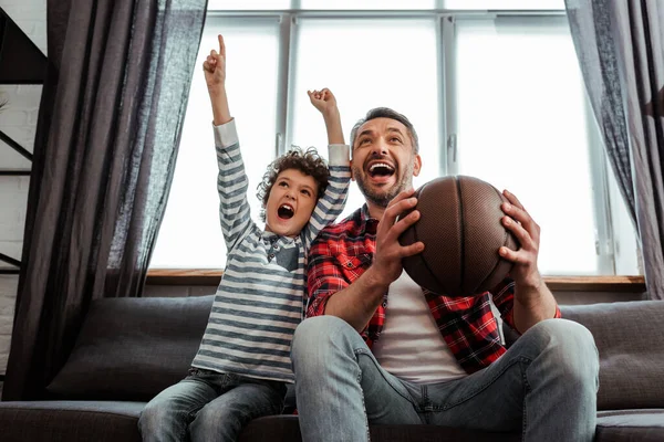 Excited kid and father holding basketball while watching championship — Stock Photo