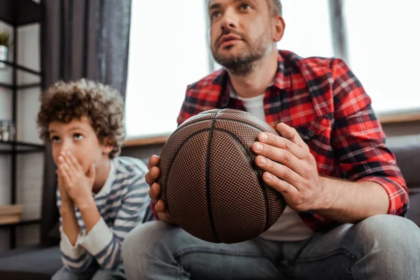 Selective focus of father holding basketball while watching championship with son — Stock Photo