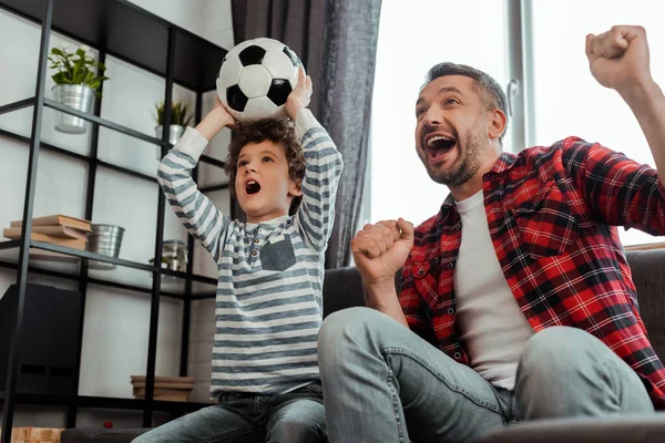 Garoto animado segurando futebol enquanto assiste campeonato com o pai — Fotografia de Stock
