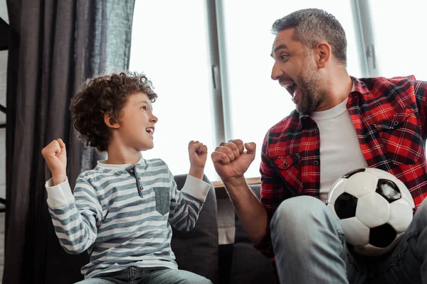 Niño alegre y padre feliz sosteniendo el fútbol mientras se miran entre sí - foto de stock