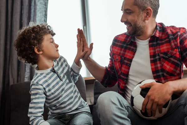 Feliz padre con el fútbol dando cinco a su hijo rizado — Stock Photo