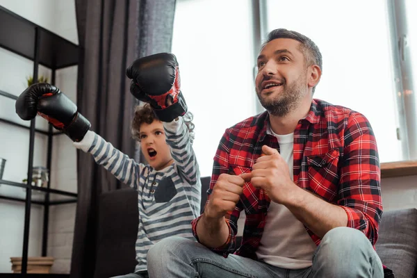 Щасливий чоловік спостерігає за чемпіонатом біля емоційного сина в боксерських рукавичках — стокове фото