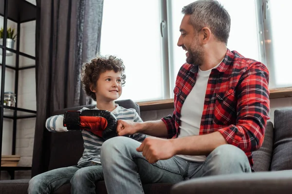 Glückliches Kind im Boxhandschuh schlägt im Wohnzimmer Fäuste mit fröhlichem Vater — Stockfoto