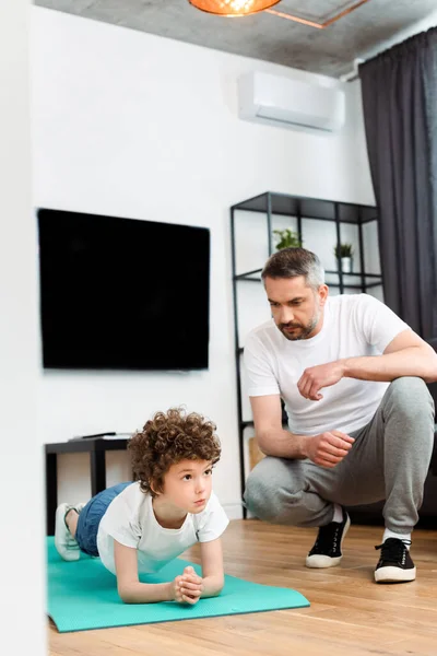 Bearded father looking at curly son working out on fitness mat — Stock Photo