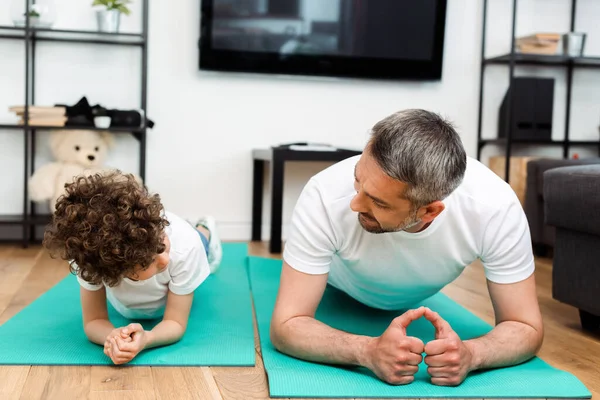 Padre barbudo e hijo rizado haciendo ejercicio sobre colchonetas de fitness - foto de stock