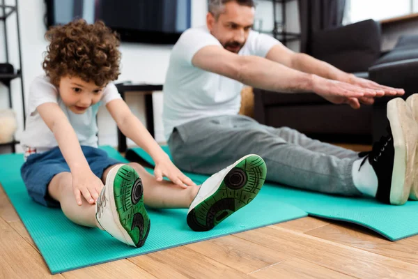 Focalizzazione selettiva del figlio riccio e del padre che si esercitano sui tappetini fitness — Foto stock