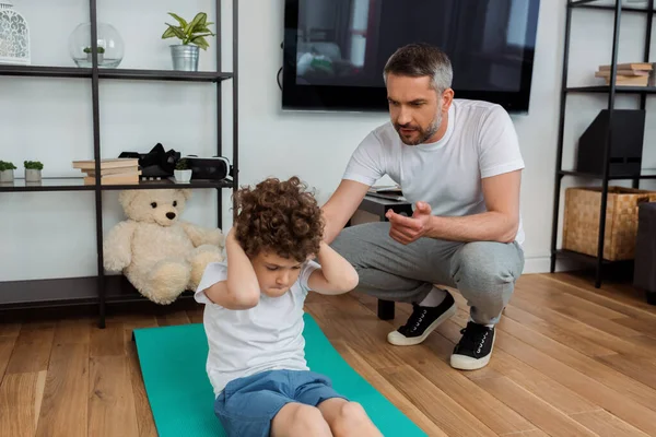 Bonito pai contando enquanto encaracolado filho exercitando no tapete de fitness — Fotografia de Stock
