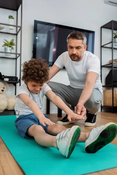 Messa a fuoco selettiva del padre bello vicino al figlio riccio che lavora sul tappeto fitness — Foto stock