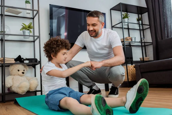 Fröhlicher Vater schlägt Fäuste mit glücklichem Sohn auf Fitnessmatte — Stockfoto