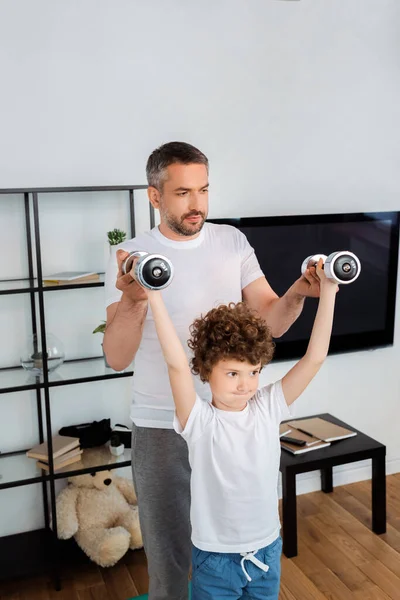 Schöner Vater hilft sportlichem Sohn beim Training mit Hanteln — Stockfoto