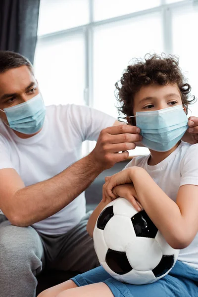 Padre cariñoso con máscara médica en el hijo rizado con el fútbol - foto de stock