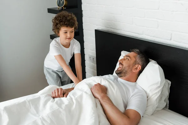 Lockiges Kind berührt glücklichen Vater, der im Bett liegt — Stockfoto