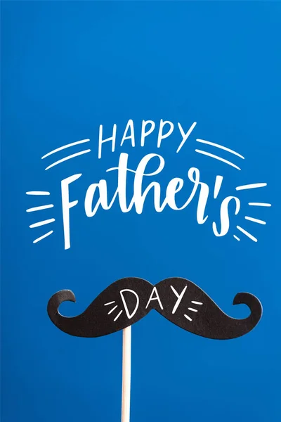 Decorative black paper crafted fake mustache on white stick isolated on blue, happy fathers day illustration — Stock Photo