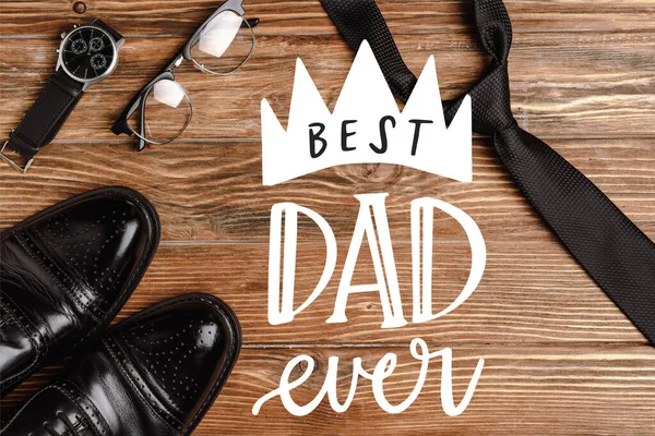 Draufsicht auf schwarze Herrenschuhe, Krawatte, Armbanduhr und Brille auf hölzernem Hintergrund, beste Papa-Abbildung aller Zeiten — Stockfoto