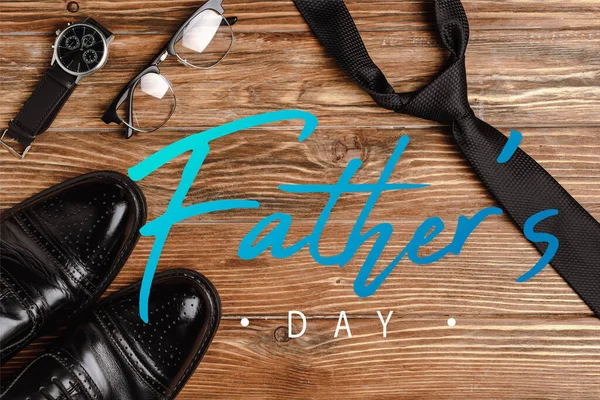 Вид сверху на черные туфли, галстук, наручные часы и очки на деревянном фоне, иллюстрация дня отца — стоковое фото