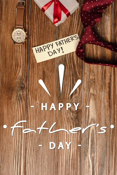Top view of gift box with red bow, greeting card with lettering happy fathers day and mens red tie and wristwatch on wooden background — Stock Photo