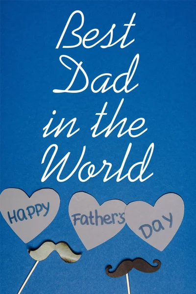 Вид зверху на декоративні чорні вуса і папір нарізані сірими серцями з написом щасливі батьки день на синьому фоні, кращий тато у світі ілюстрація — стокове фото