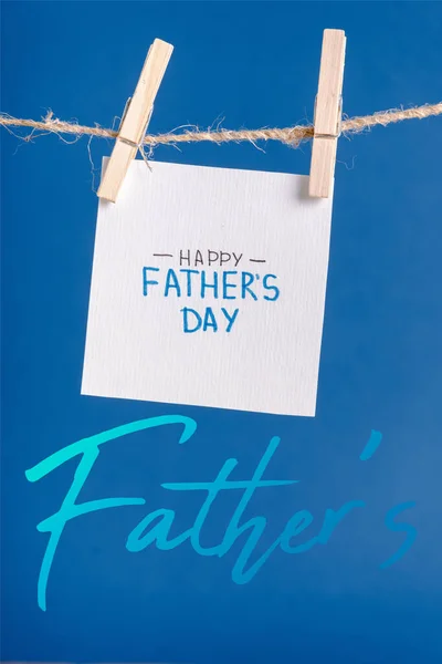 White paper with lettering happy fathers day hanging on rope with clothespins isolated on blue — Stock Photo