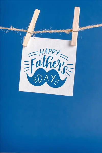 White paper with lettering happy fathers day hanging on rope with clothespins isolated on blue — Stock Photo