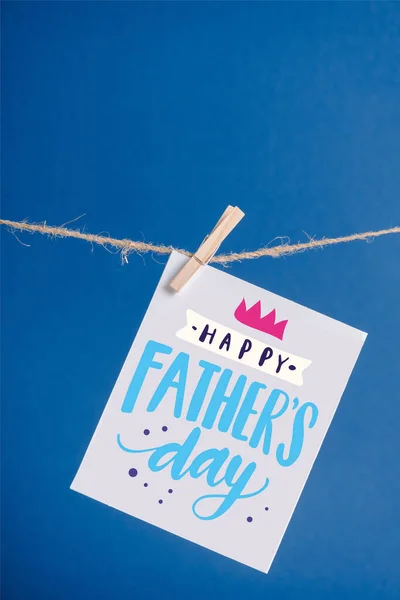 White greeting card with happy fathers day illustration hanging on rope with clothespins isolated on blue — Stock Photo