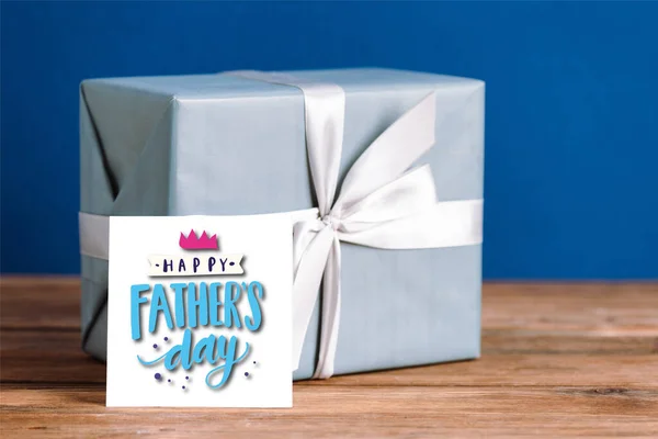 Selektiver Fokus der Grußkarte mit Illustration zum Vatertag und Geschenkbox mit weißer Schleife isoliert auf blau — Stockfoto