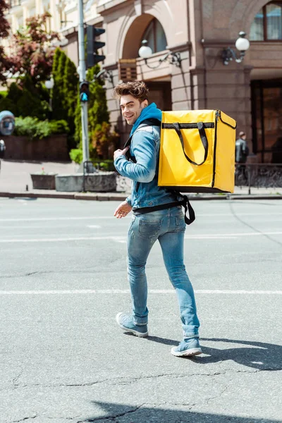 Vue arrière du courrier souriant avec sac à dos regardant la caméra sur le passage supérieur — Photo de stock