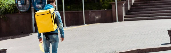 Panoramic crop of delivery man with thermo backpack walking on urban street — Stock Photo