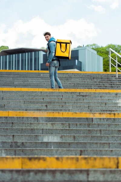 Selective focus of courier smiling at camera while standing on stairs — Stock Photo