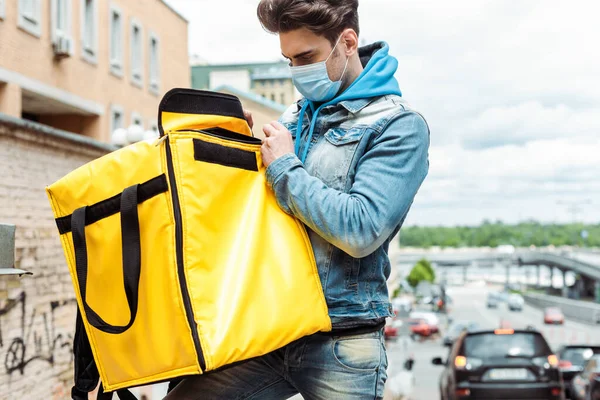 Courrier en masque médical tenant sac thermo dans la rue urbaine — Photo de stock