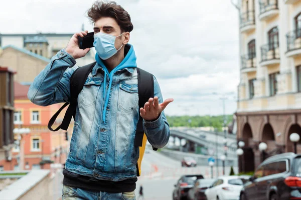 Entrega hombre en máscara médica hablando en el teléfono inteligente cerca de la carretera en la calle urbana - foto de stock