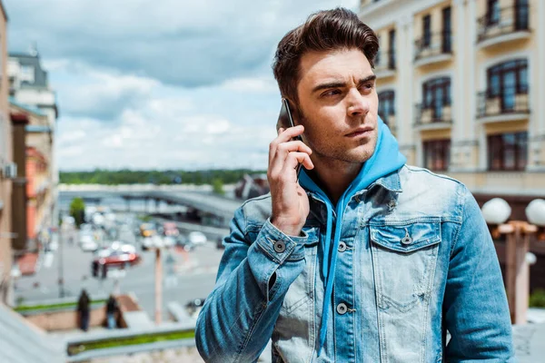 Красивый мужчина разговаривает по смартфону с городской улицей на заднем плане — стоковое фото