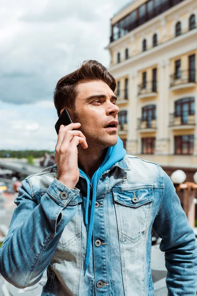 Handsome man in denim jacket talking on smartphone on urban street — Stock Photo