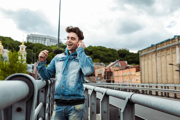 Enfoque selectivo del hombre sonriente usando auriculares en la calle urbana - foto de stock