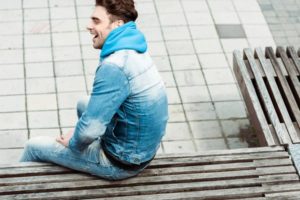 Hochwinkelaufnahme eines positiven Mannes, der auf einer Holzbank in der städtischen Straße sitzt — Stockfoto