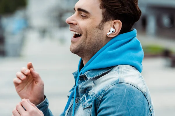 Side view of happy man listening music in earphones on urban street — Stock Photo