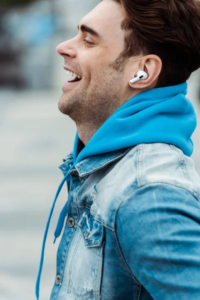 Side view of happy man in earphones laughing outdoors — Stock Photo