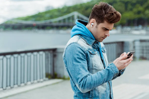 Young man using earphones and cellphone on urban street — Stock Photo