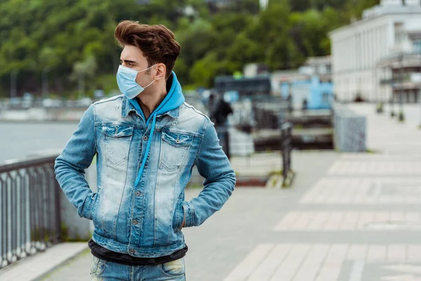 Молодий чоловік у медичній масці, дивлячись на міську вулицю — стокове фото