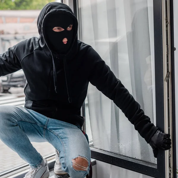 Robber en gant de cuir et cagoule debout près de la fenêtre ouverte — Photo de stock