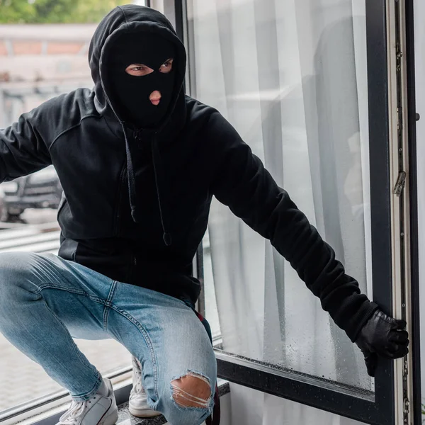 Räuber mit Lederhandschuhen und Sturmhaube steht am offenen Fenster — Stockfoto