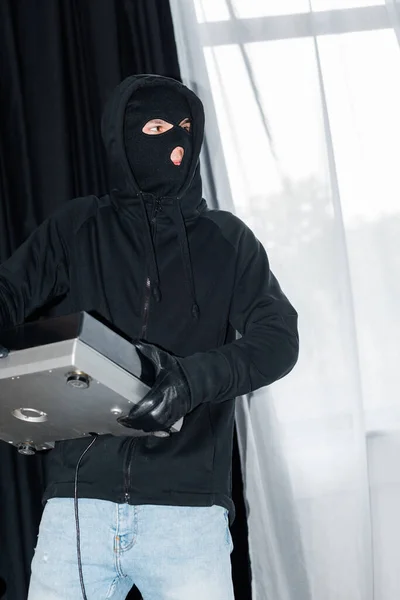 Ladrón en pasamontañas y guante de cuero sosteniendo tocadiscos durante robo - foto de stock