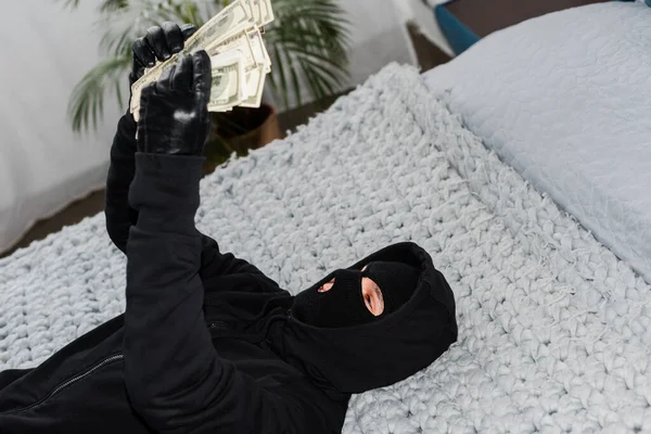 Selective focus of thief in mask and leather gloves counting dollar banknotes on bed — Stock Photo