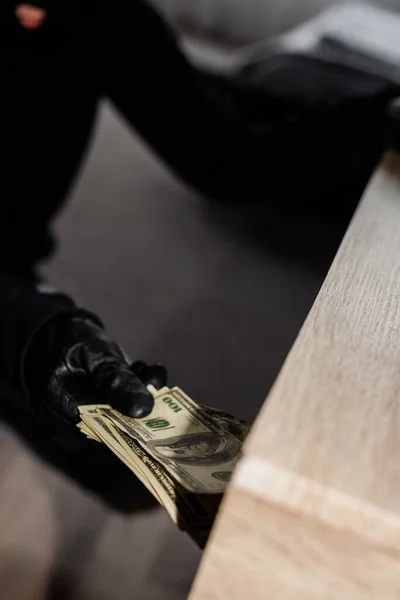 Selective focus of robber in leather glove taking dollars from table — Stock Photo