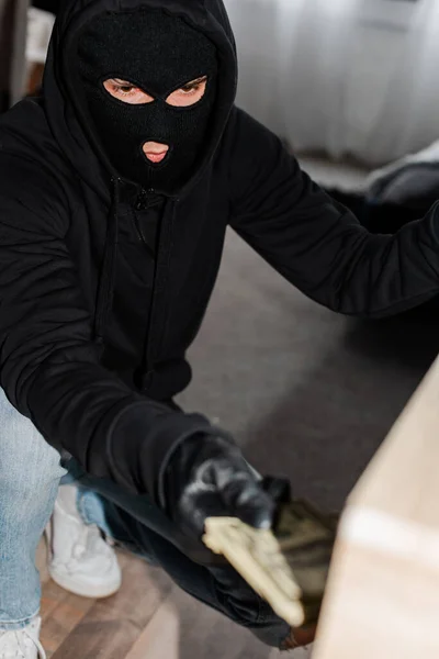 Selective focus of thief in mask taking dollar banknotes from table during robbery — Stock Photo