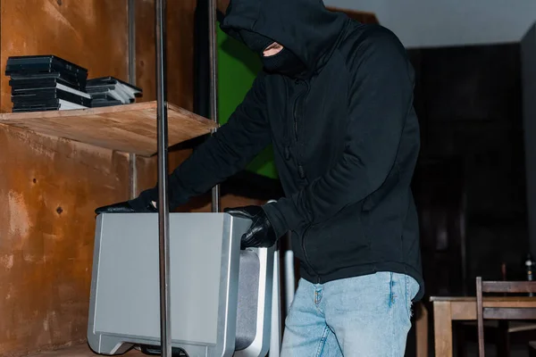 Ladrão em balaclava levando alto-falante sem fio do armário durante o roubo — Fotografia de Stock